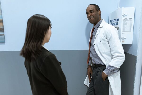 A physician in a white coat talking with a patient in a clinic hallway