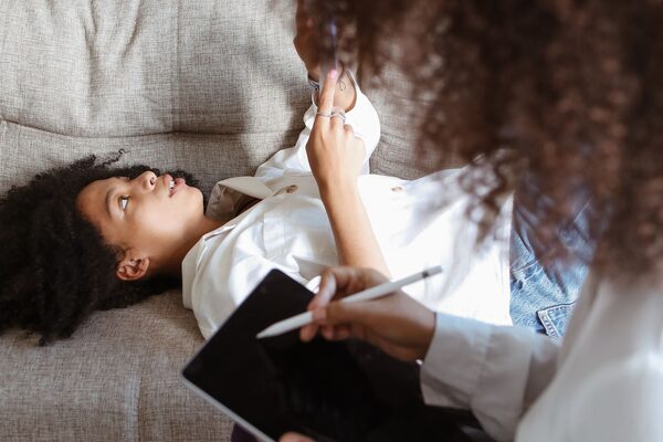 A woman resting on a couch during a session while a clinician takes notes